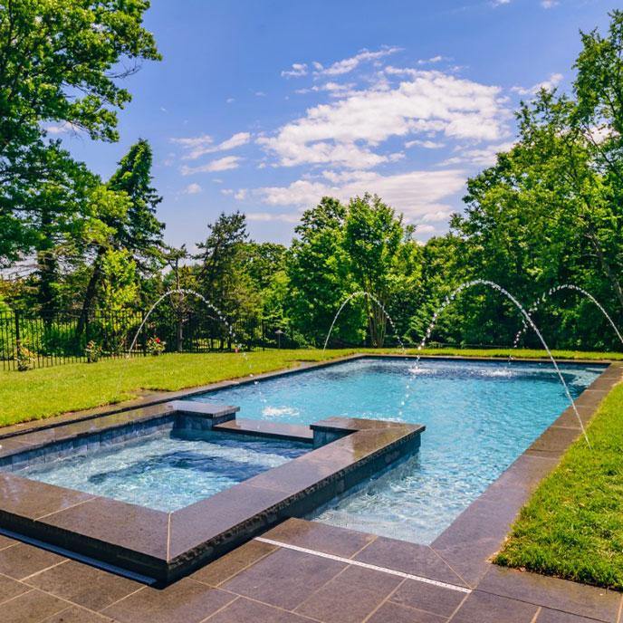 rectangular pool with natural stone and pool deck with spa and outdoor kitchen