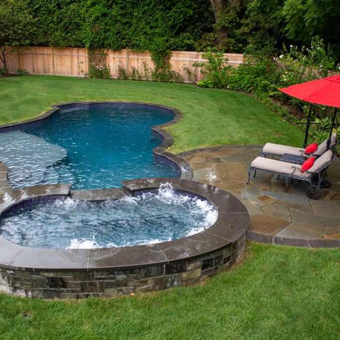 pool surrounded by green grass and lounge chairs with red pillows and umbrella