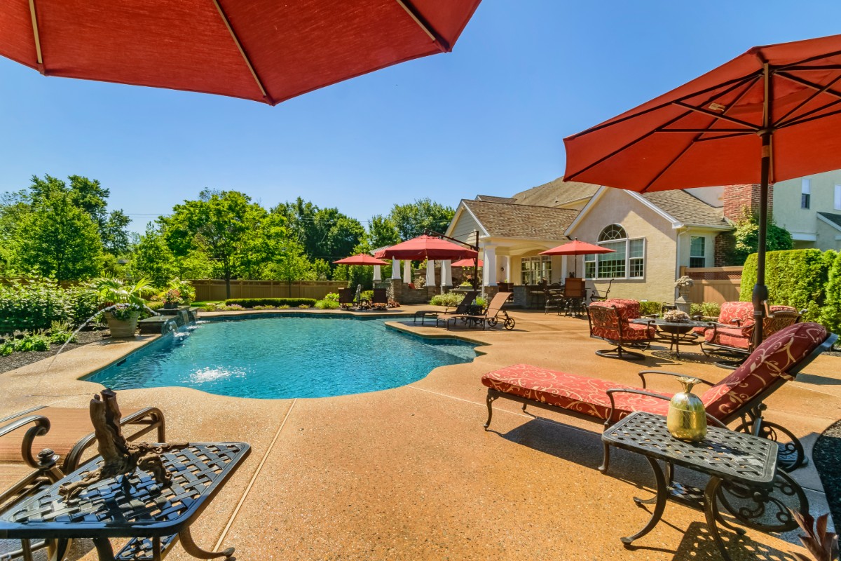 pool area with natural stone fireplace and outdoor dining area with red upholstery and umbrellas